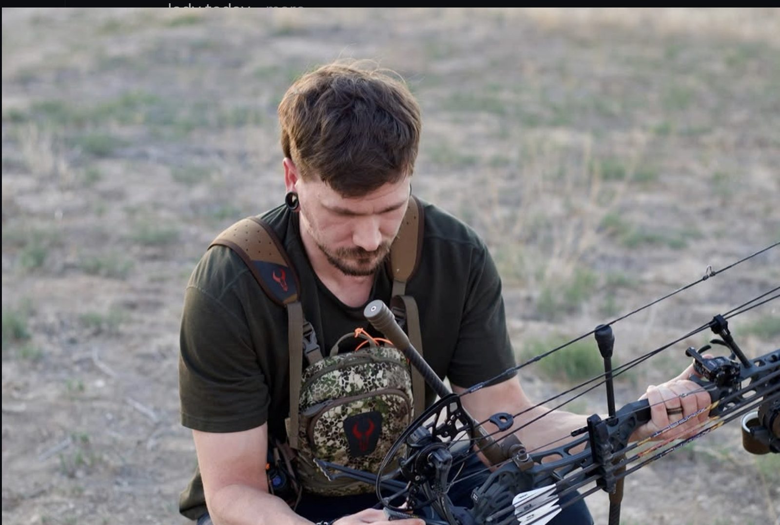 Skyler kneeling in a field, checking the string on his compound bow